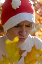 A woman in a hat of Santaclaus with a sly evil face among the autumn foliage as a harbinger of the coming winter.