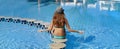 Woman in hat sits on the edge of stone in the middle of the swimming pool spa. Beautiful exotic hotel relax. Panoramic banner