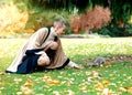 Woman in hat sitting on the autumn leaves and feeding squirell in the park