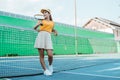 woman in hat and sportswear holding racket leaning on net Royalty Free Stock Photo