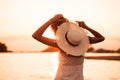 A woman with a hat at sunset in profile. A young blonde in a white dress and a straw hat decorated with a ribbon and Royalty Free Stock Photo