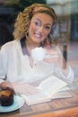 Woman having coffee while reading book seen through cafe window Royalty Free Stock Photo