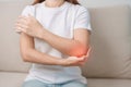 Woman having elbow ache during sitting on couch at home, muscle pain due to lateral epicondylitis or tennis elbow. injury, Health