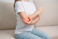 Woman having elbow ache during sitting on couch at home, muscle pain due to lateral epicondylitis or tennis elbow. injury, Health