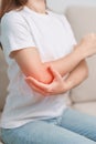 Woman having elbow ache during sitting on couch at home, muscle pain due to lateral epicondylitis or tennis elbow. injury, Health