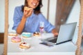 A woman is having a good time while eating delicious donuts and using a laptop in a pastry shop. Pastry shop, dessert, sweet Royalty Free Stock Photo