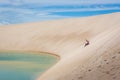 Woman having a good time, rolling down a huge sand dune in a amazing scenario, natural pool lagoon in the bottom. North of Brasil,