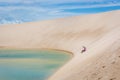 Woman having a good time, rolling down a huge sand dune in a amazing scenario, natural pool lagoon in the bottom. North of Brasil,