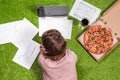 Woman having lunch with pizza and glass of wine working on the grass using laptop with graphics and charts printed on the paper.