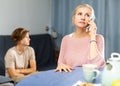 Woman having phone conversation at home against background of upset teenage son Royalty Free Stock Photo