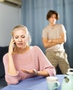 Woman having phone conversation at home against background of upset teenage son Royalty Free Stock Photo