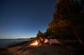 Woman having a rest at night camping near tourist tent, campfire on sea shore under starry sky Royalty Free Stock Photo