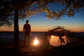 Woman having a rest at night camping near tourist tent, campfire on sea shore under starry sky Royalty Free Stock Photo