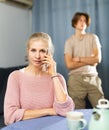 Woman having phone conversation at home against background of upset teenage son Royalty Free Stock Photo