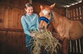 Woman, hay and feeding horse in stable, barn and rancher of farming animals in sustainable shed. Happy female farmer Royalty Free Stock Photo