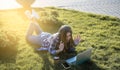 Woman in headphones having a video call with laptop, lying on the grass outside in park. Happy and smiling girl Working and Royalty Free Stock Photo
