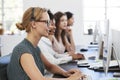 Woman with headset at computer in office beside colleagues