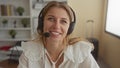 Woman with headset microphone smiling and speaking in an office building with headset mic visible; friendly remote support Royalty Free Stock Photo