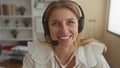 Woman with headset microphone smiling and speaking in an office building with headset mic visible; friendly remote support Royalty Free Stock Photo