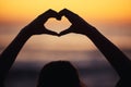 Woman, heart hand and shadow at sunset at beach and ocean with peace and zen hands sign. Silhouette, nature and sea on a Royalty Free Stock Photo