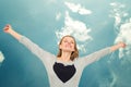 Woman with heart raising arms above head and sky