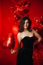 Woman with Hearts Balloons on a red background. Beauty Girl on Valentine`s Day. Model in a stylish black dress