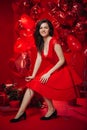 Woman with Hearts Balloons on a red background. Beauty Girl on Valentine`s Day. Model in a stylish red dress