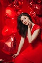 Woman with Hearts Balloons on a red background. Beauty Girl on Valentine`s Day. Model in a stylish red dress