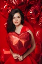 Woman with Hearts Balloons on a red background. Beauty Girl on Valentine`s Day. Model in a stylish red dress