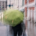 Woman with a heavy bag under the green umbrella, cold rainy weather, abstract, blurred image