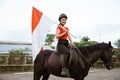 woman in a helmet riding a horse carrying Indonesian flag