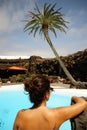 A woman on her back slightly unfocused facing an idyllic landscape with a palm tree over a design  pool in Jameos del Agua in Royalty Free Stock Photo