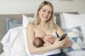 Woman in her bedroom on the white cushions, smiling and breastfeed her baby.