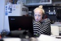 Adult woman in her casual home clothing working and studying remotely from her small flat late at night.