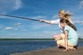 Woman with her daughter is fishing on the pier in sunny weather Royalty Free Stock Photo