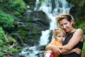 Woman with her daughter standing near the waterfall in the mountains of the Carpathians and rest after a summer forest trip