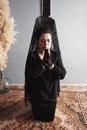 Woman on her knees with a veil and a black suit praying with a rosary