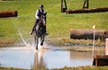 Horse with rider in an eventing tournament galloping through the water to the next jump. Royalty Free Stock Photo