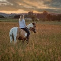 Blonde woman with horse at dawn on a large summer meadow.