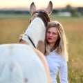 Blonde woman with horse at dawn on a large summer meadow.