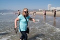 Woman in her 60s walks along the shoreline in Santa Monica California, having a fun time with her shoes off