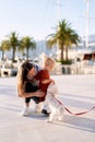 Woman and her toddler are petting a small white dog on a boat pier Royalty Free Stock Photo