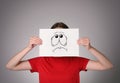 Woman hiding behind sheet of paper with anxious face on grey background