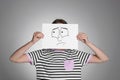 Woman hiding behind sheet of paper with sad face on grey background Royalty Free Stock Photo