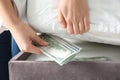 Woman hiding dollar banknotes under mattress in bedroom, closeup