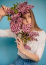 Woman hiding head in bouquet lilac flowers over colorful blue background Royalty Free Stock Photo