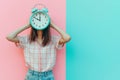 Woman hiding her face with alarm clock. Time management, schedule, deadline, time concept. Flow of time, rush and hurry, timing,