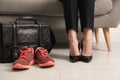 Woman in high heel shoes sitting on sofa near comfortable sneakers in office, closeup Royalty Free Stock Photo