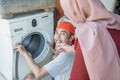Woman in the hijab looks at the washing machine being repaired by an electronics repairman