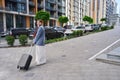 Woman stands on a deserted street holding a suitcase on wheels